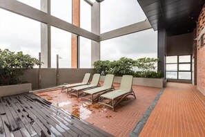 Een terras op het dak met ligbedden en een natte vloer, wat duidt op regen.