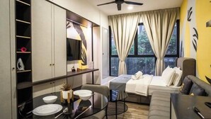 Une chambre d’hôtel moderne équipée d’un lit, d’un canapé, d’une table à manger avec des chaises, d’un ventilateur de plafond et d’une grande fenêtre avec des rideaux.