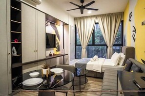 Una habitación de hotel moderna con cama, sofá, mesa de comedor con sillas, ventilador de techo y un ventanal con cortinas.