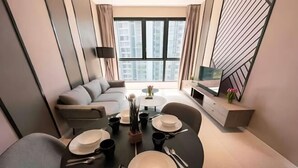 Una sala de estar moderna con comedor, un sofá, un televisor y vistas de edificios a través de amplios ventanales.