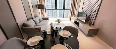 Ein modernes Wohnzimmer mit Essbereich, einer Couch, einem Fernseher und Blick auf Gebäude durch große Fenster.