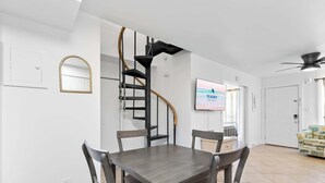 Ein Essbereich mit Wendeltreppe, einem an der Wand befestigten Fernseher und einer Tür zu einem weiteren Zimmer.