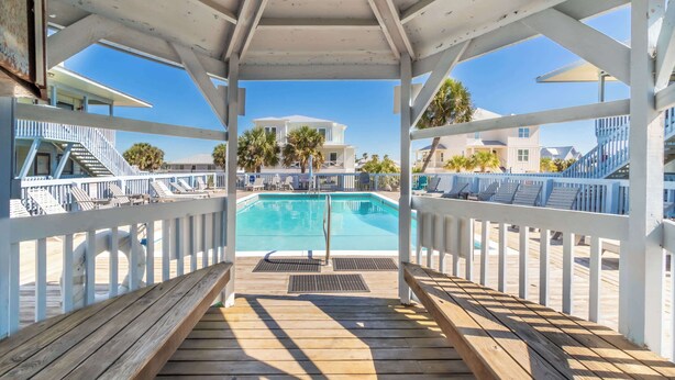 Eine Holzterrasse mit Pool, weißen Geländern und freiem Blick auf ein weißes Gebäude im Hintergrund.