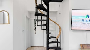 Eine Wendeltreppe in einer Diele, ein Fernseher zeigt eine Strandansicht.