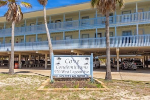 A multi-story building with balconies, a sign indicating 'Cove Condominiums 920 West Lagoon Ave. NO PETS ALLOWED,' and a parking area with vehicles.