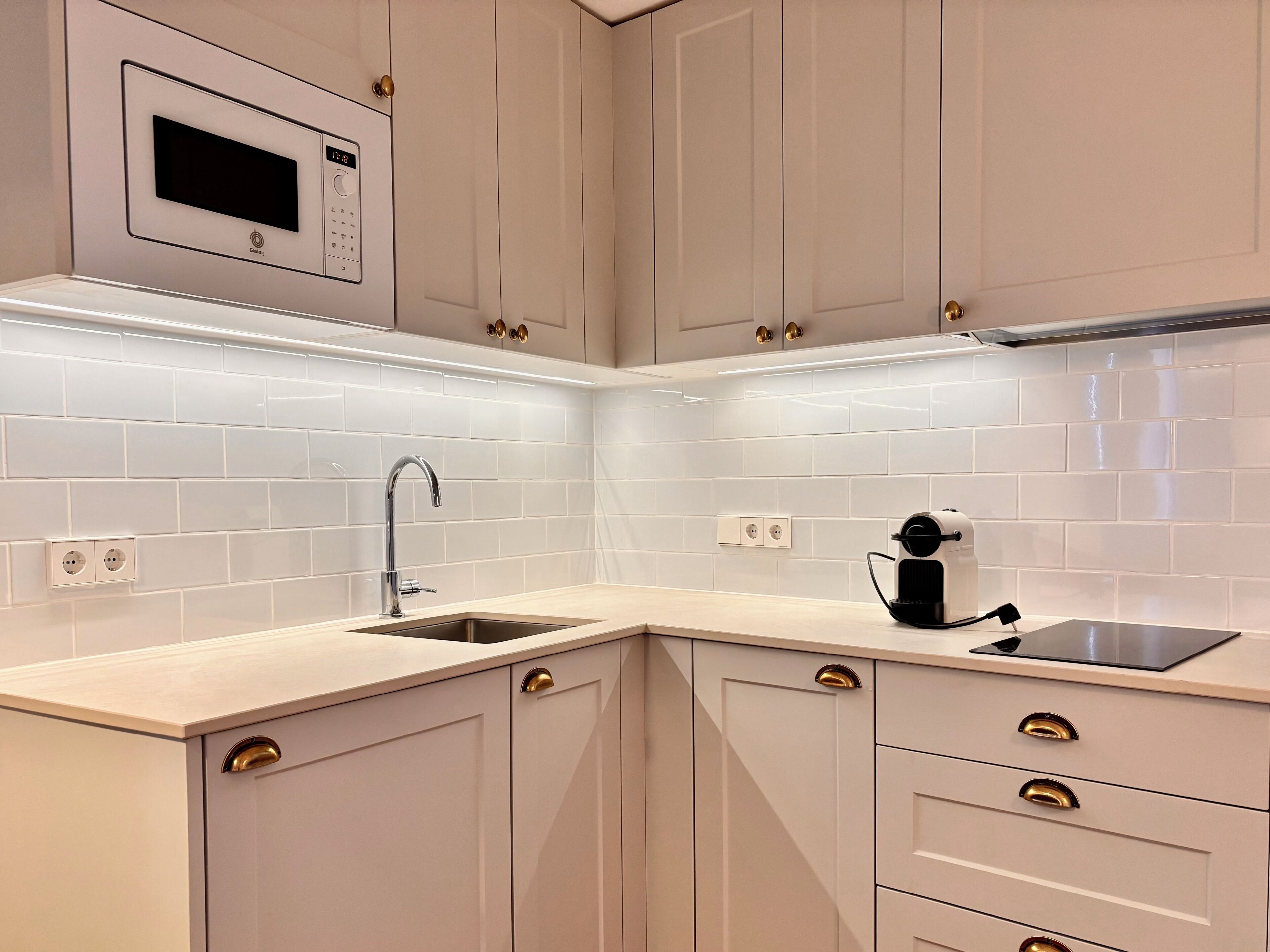Una cocina moderna con microondas integrado, pileta de acero inoxidable y cafetera.