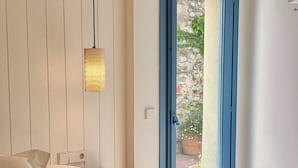 Un dormitorio con cama, mesita de noche, lámpara de pared y puerta que da a un espacio exterior con pared de piedra y plantas en macetas.