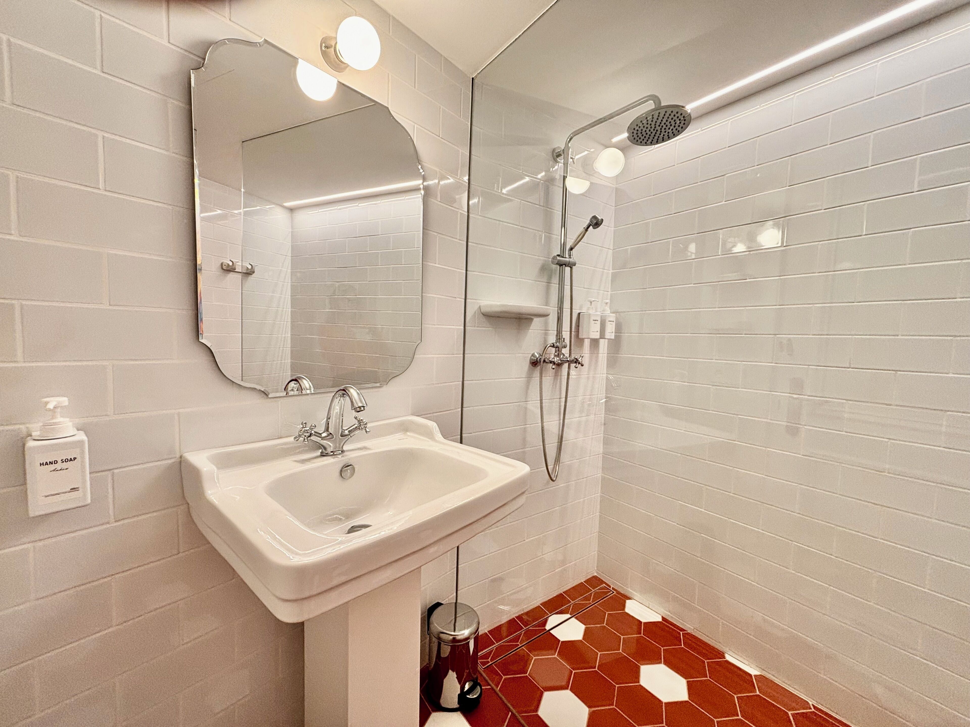 Un baño con un lavamanos blanco, un espejo, una ducha y un suelo de baldosas rojas.