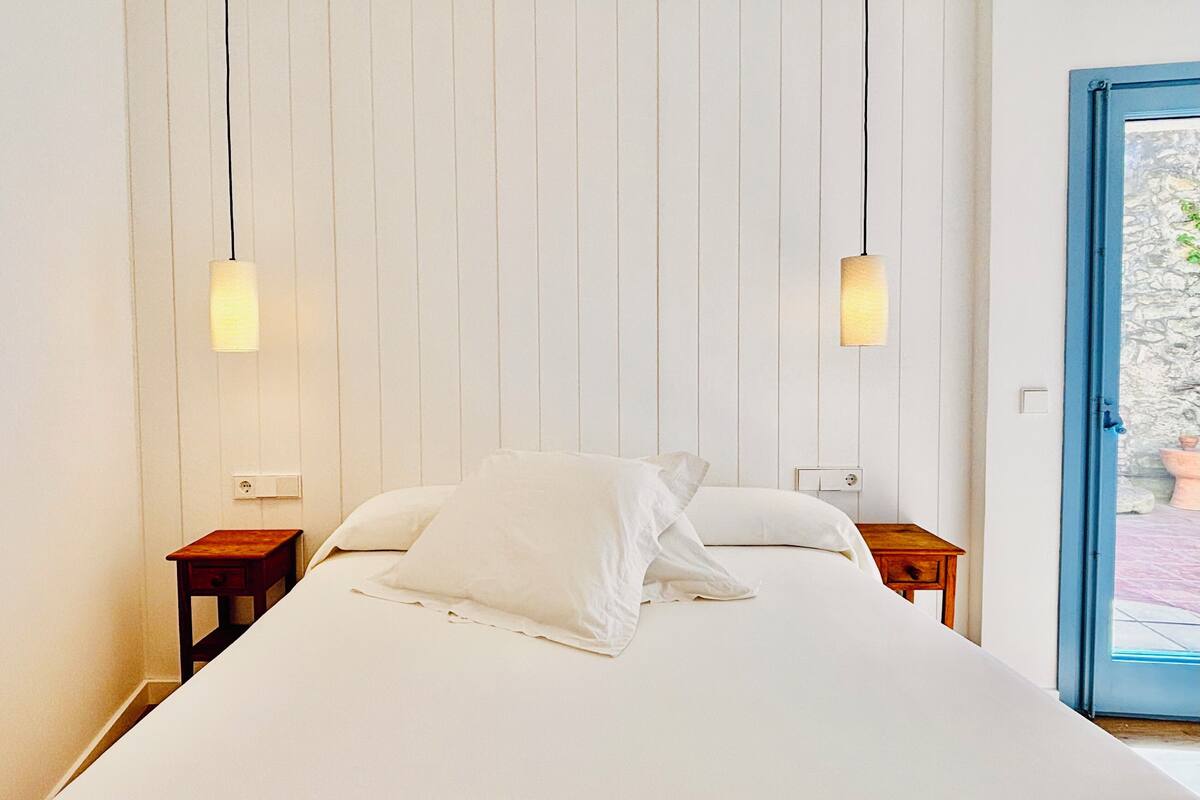 A bedroom with a large bed, two bedside tables, and a door leading to an outdoor area.