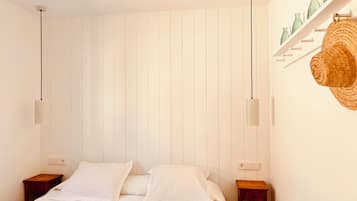 A bedroom with a bed, two bedside tables, a wall-mounted shelf with bottles, and two pendant lights.