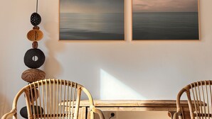 Una habitación con dos obras de arte enmarcadas que muestran un cielo nublado sobre el agua, un objeto decorativo en la pared y una mesa de madera con sillas.