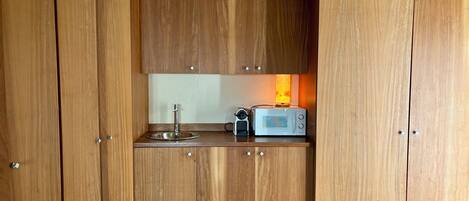 A compact kitchen with wooden cabinets, a stainless steel sink, and a microwave.