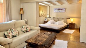Un dormitorio con cama, una mesita de centro de madera, un sofá con cojines estampados, una mesita de noche y una lámpara.