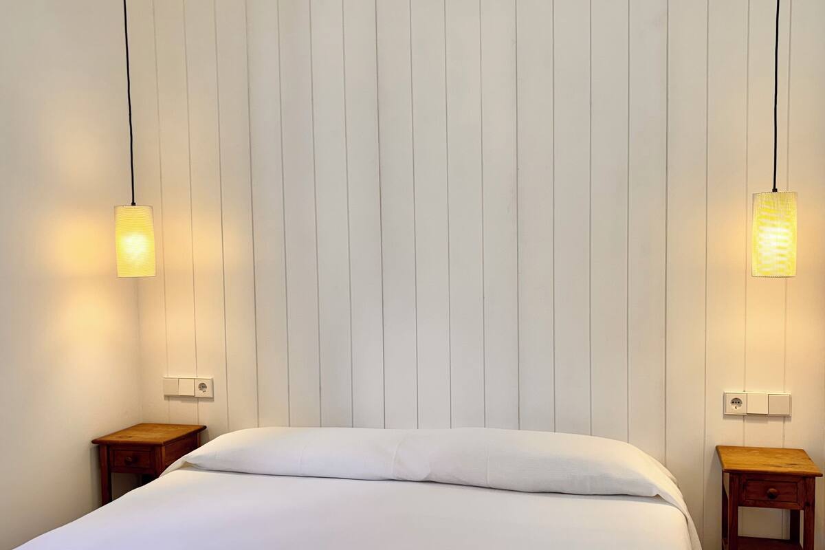 A room with a bed, two nightstands, and two hanging lamps.