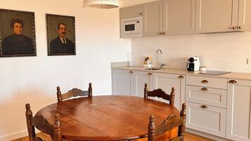 A dining area with a wooden table and chairs, a kitchen with light grey cabinets, a white pendant light, and a microwave.