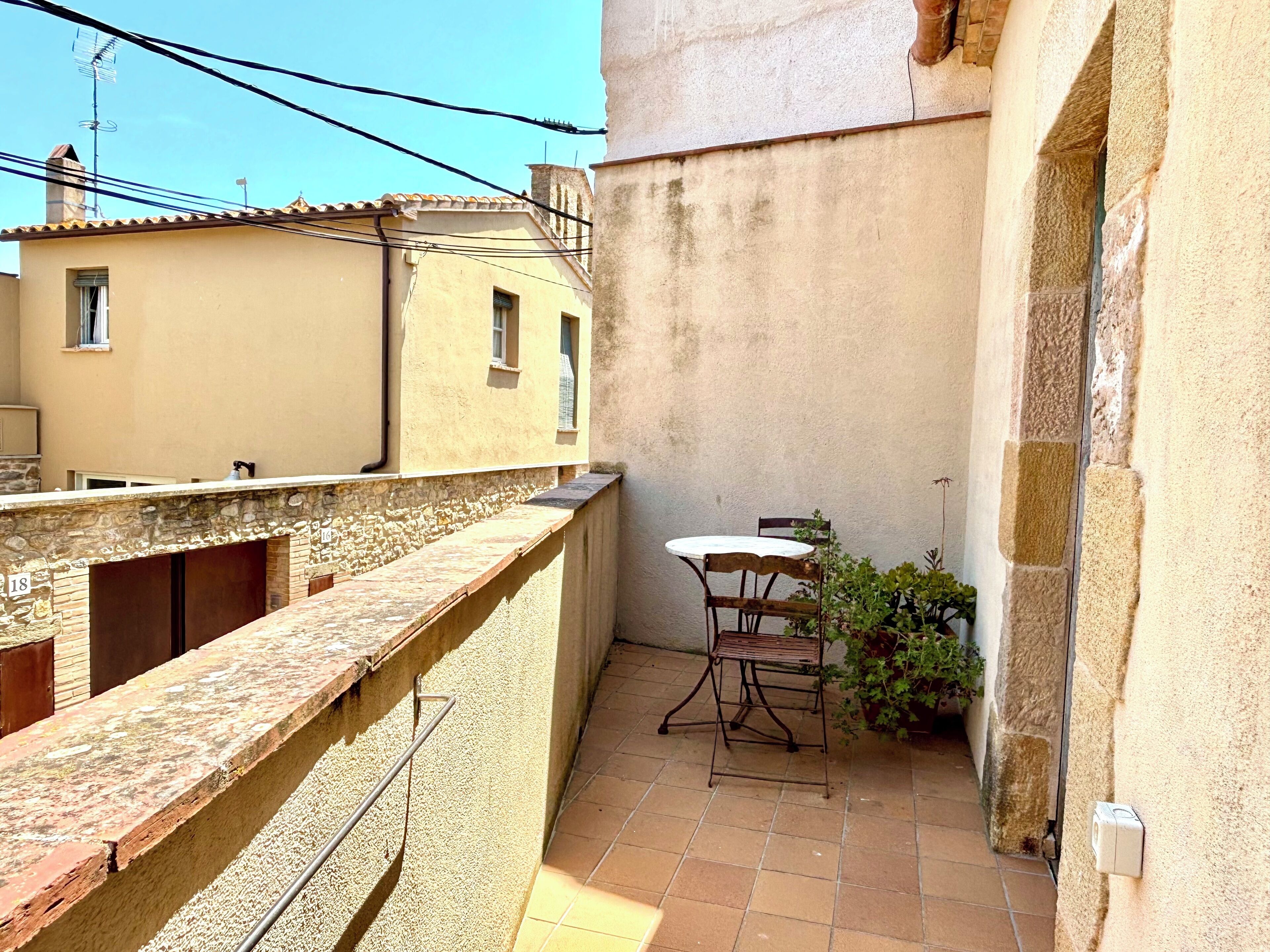 A small outdoor patio with a table and chairs, a stone wall, and a view of neighboring buildings.