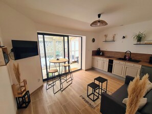 Una cocina moderna con comedor, televisor montado en la pared y un amplio ventanal corredero que da a un balcón.