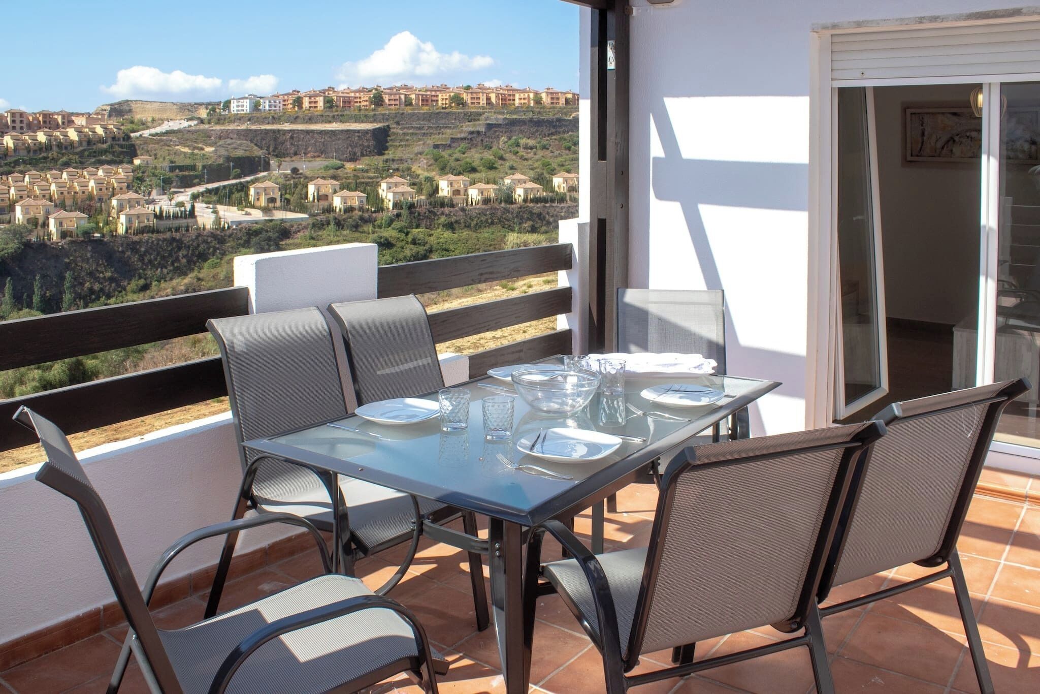 Un balcón con una mesa preparada para dos, con vistas a una ladera llena de edificios.