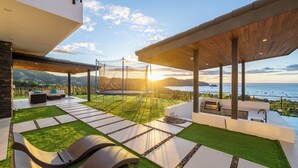 Une terrasse extérieure moderne avec vue sur l’océan, un espace barbecue et des chaises longues.