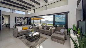 Un salon moderne avec un canapé d’angle, une table basse et une grande fenêtre donnant sur un paysage magnifique.