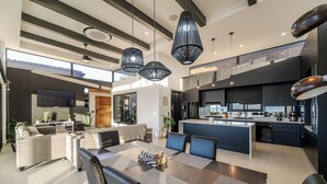 Une cuisine moderne avec des meubles de couleur sombre, un îlot central et un coin repas comprenant une grande table et des chaises.