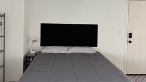 Ein Schlafzimmer mit einem Bett, einem Nachttisch mit Lampe, einem Kleiderschrank und einer Tür.
