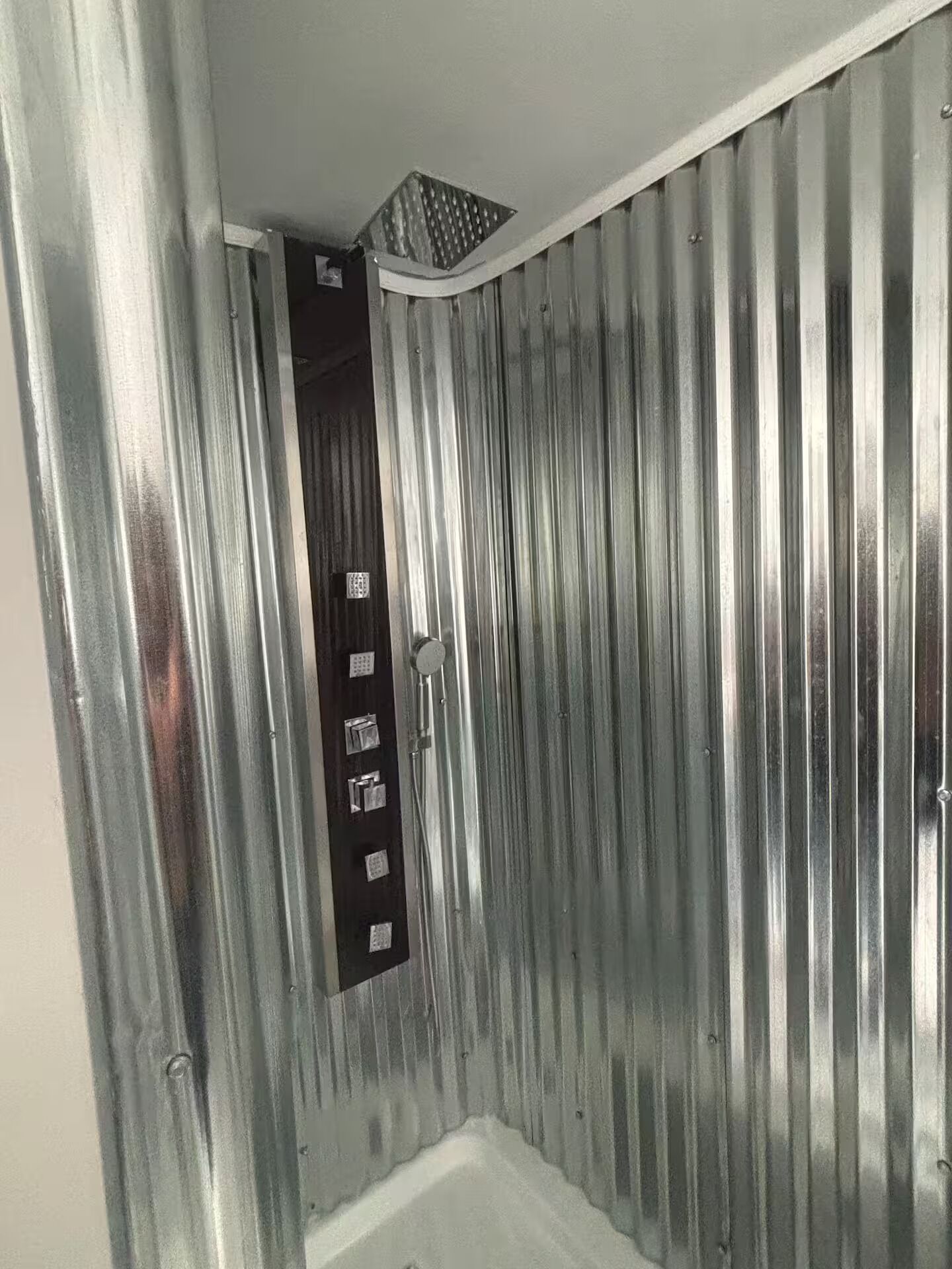 Ett badrum med en duschhörna, en dörr med en kontrollpanel och ett ventilationssystem.
