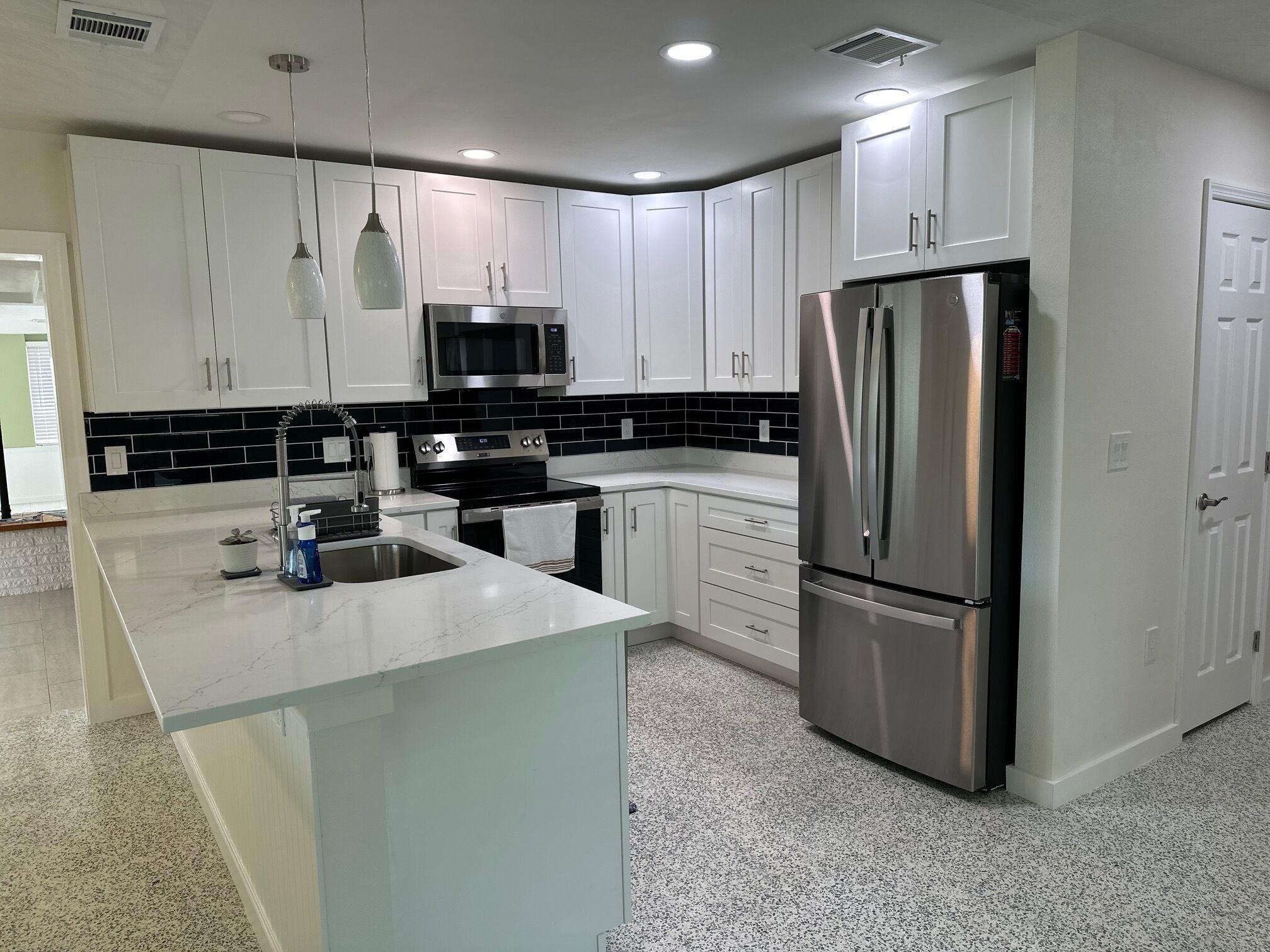 A modern kitchen with white cabinets, a stainless steel refrigerator, a microwave, and a granite countertop.