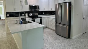 Eine moderne Küche mit weißen Schränken, einem Edelstahl-Kühlschrank, einer Mikrowelle und einer Arbeitsplatte aus Granit.