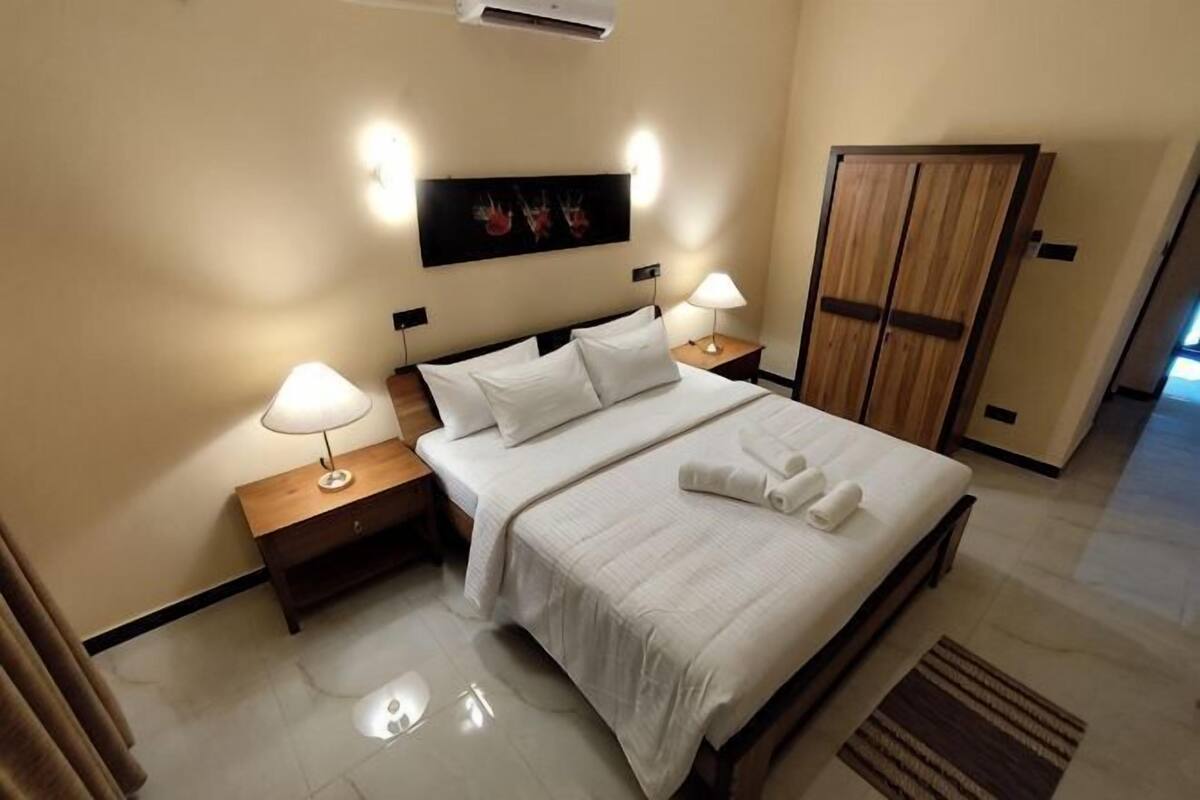 A hotel room with a bed, nightstands, lamps, a wardrobe, and a painting on the wall.