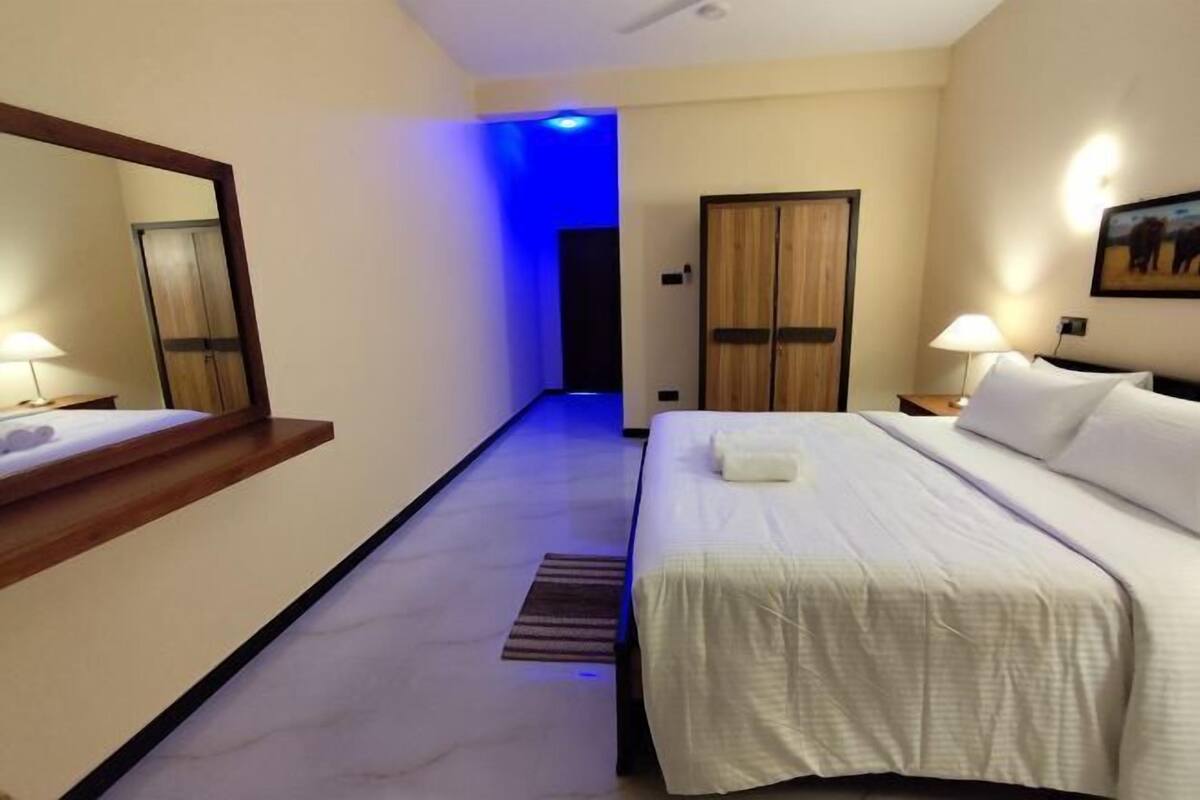 Et hotelværelse med seng, spejl, natbord, lampe og dør.