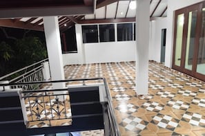 A covered outdoor area with a checkered floor, a staircase with a metal railing, and a view of a building with windows and a door.