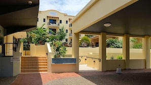 A hotel entrance with a reception desk, a staircase leading to the building, and a covered outdoor area with plants. - Beachfront Apartment in Townsville 1BR on The Strand with Pool and Parking (Townsville)