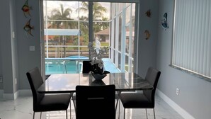 A dining area with a glass table and chairs, a chandelier, and decorative fish on the wall. - 4-bedroom, pool, fishing, games, BBQ, kayak and front water. (Cape Coral)