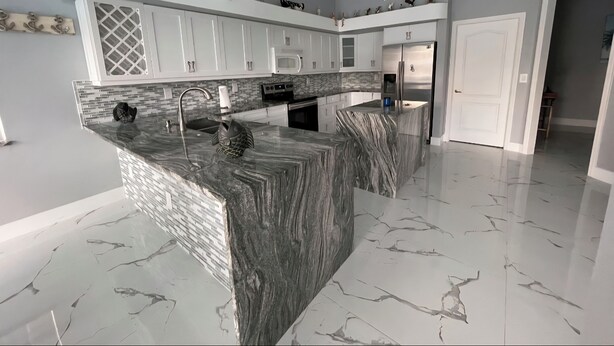 A modern kitchen with white cabinets, a marble island, and a ceiling fan. - 4-bedroom, pool, fishing, games, BBQ, kayak and front water. (Cape Coral)