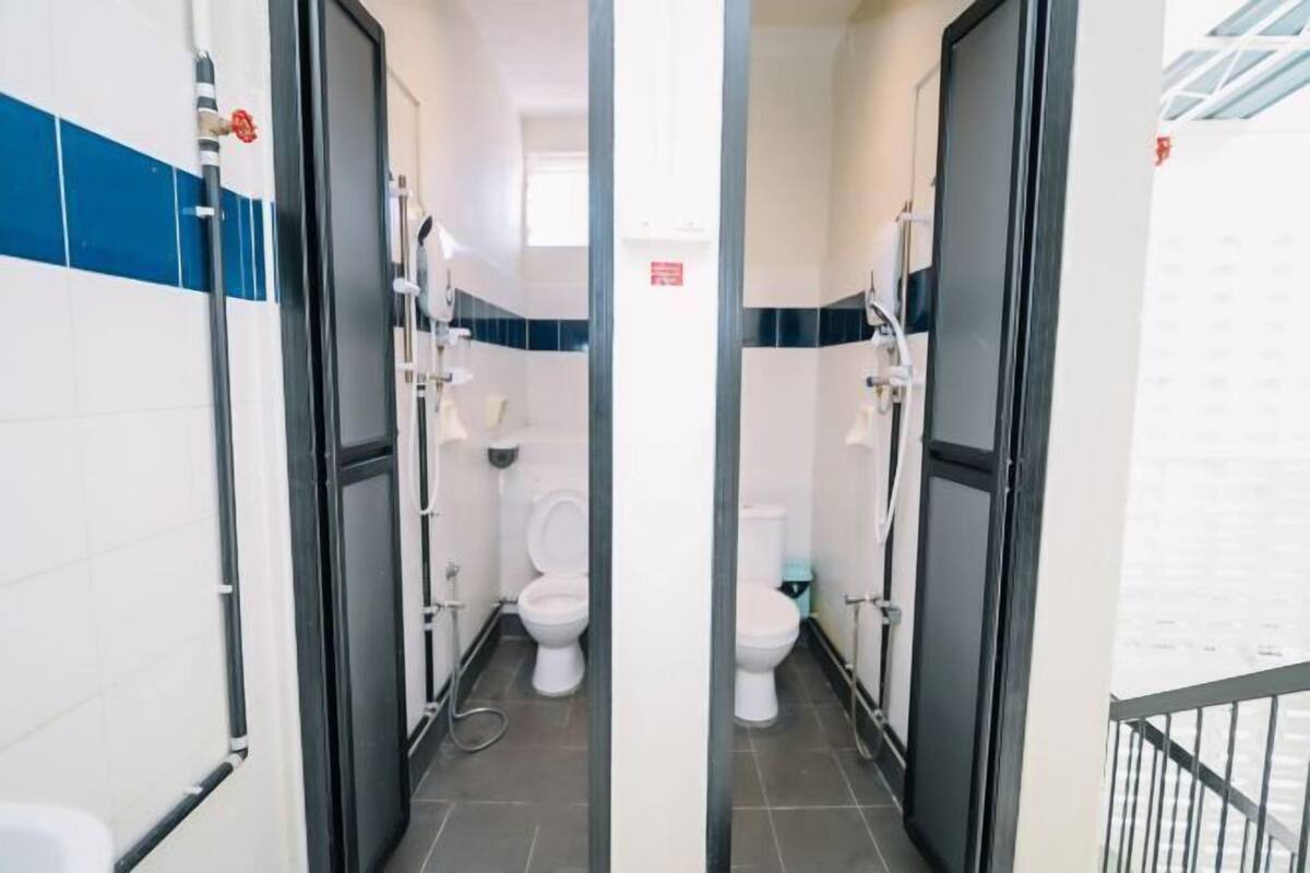 A narrow hallway with two toilets, a visible pipe, and a metal railing on the right.