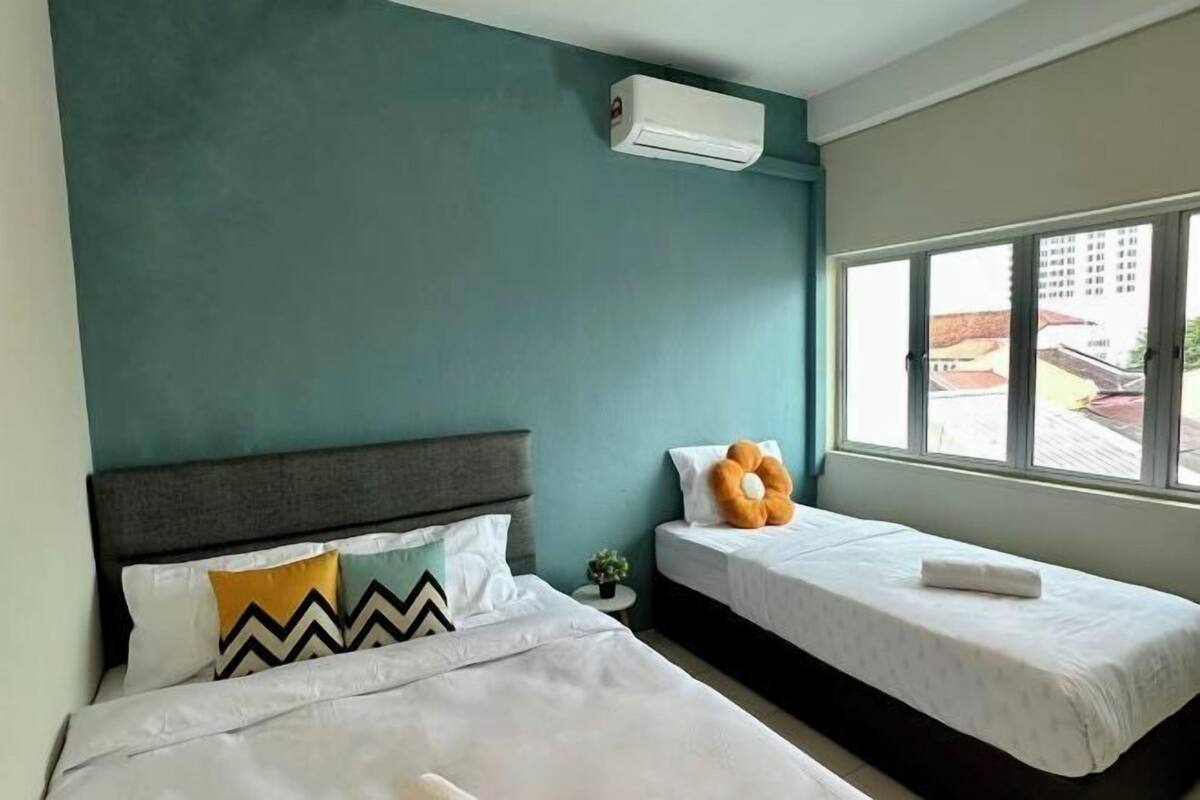 A hotel room with two beds, a window, and an air conditioning unit.