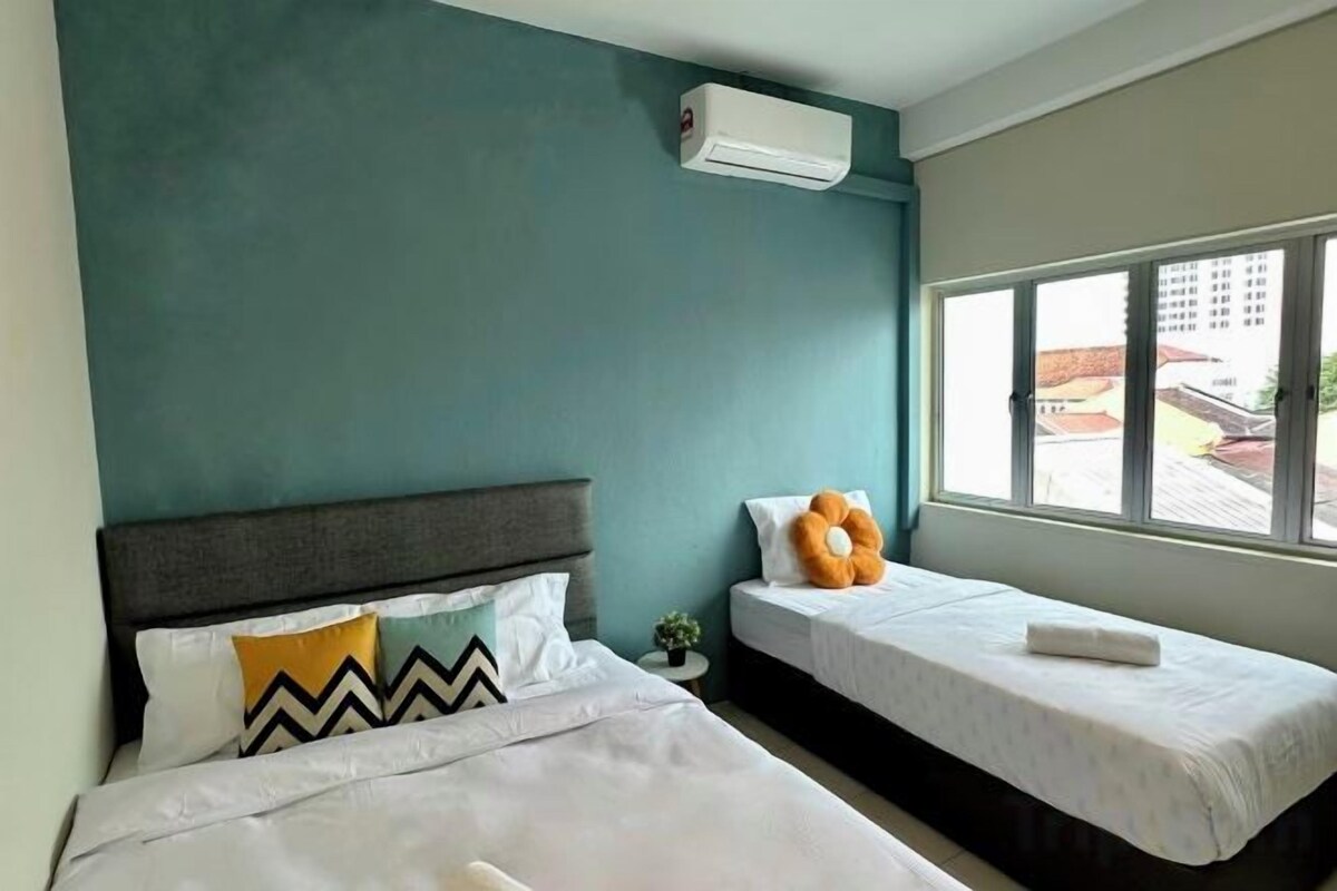 A hotel room with two beds, a window with a view, and an air conditioning unit.