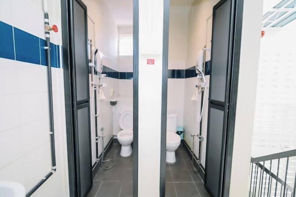 A narrow hallway with two toilets, each with a bidet attachment, and a visible water pipe on the left.