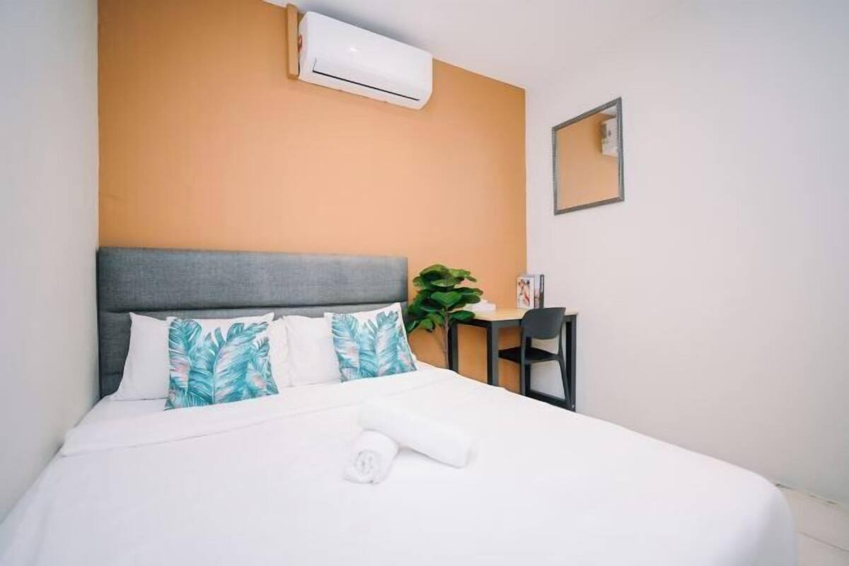 A hotel room with a bed, a desk, an air conditioner, and a mirror.