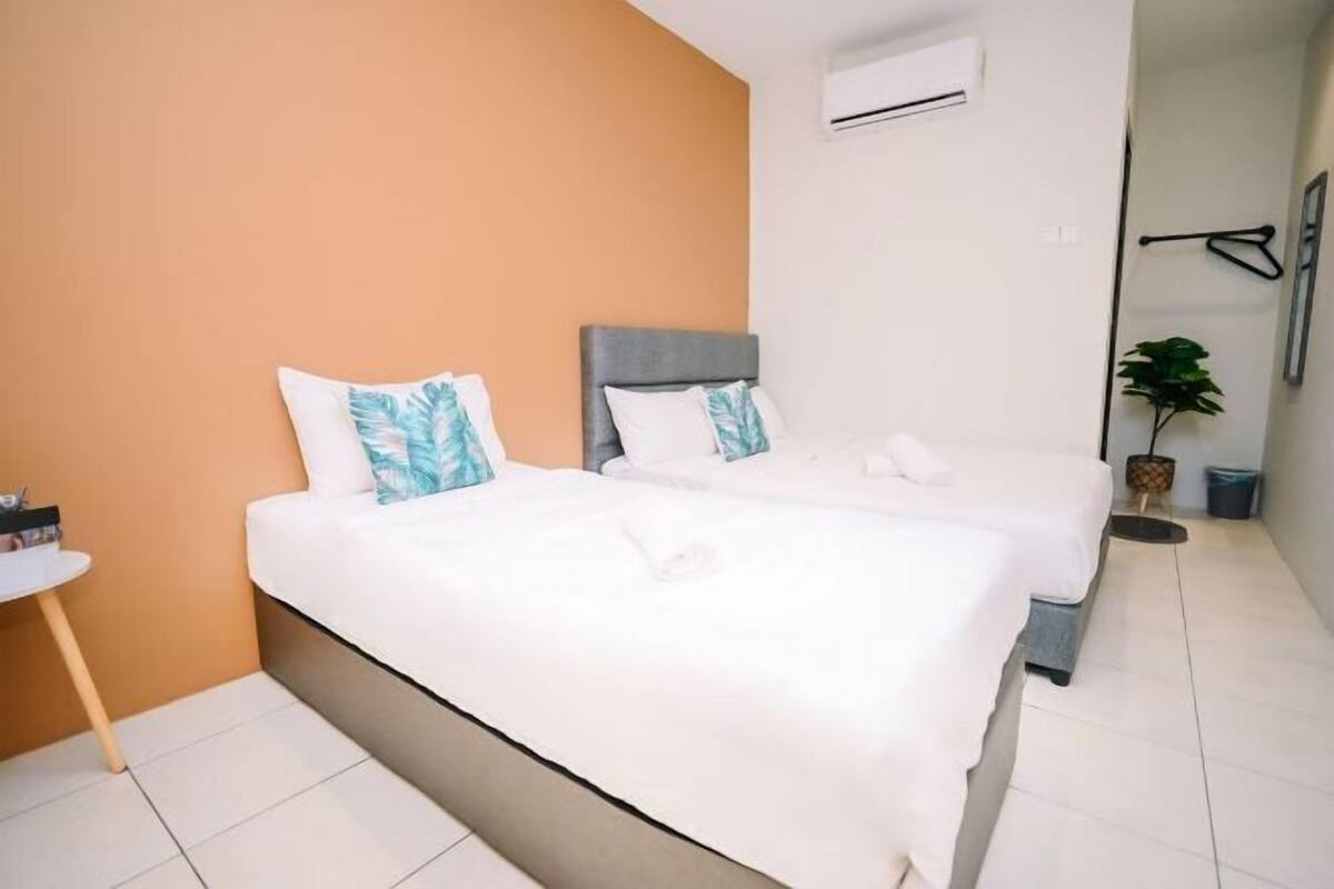 A hotel room with two beds, a small table, an air conditioning unit, and a potted plant.