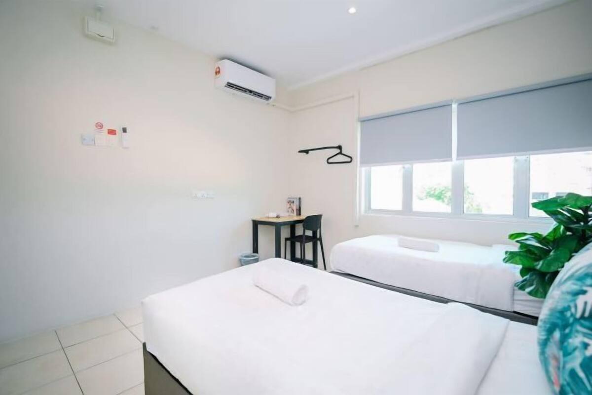 A hotel room with two beds, a desk, a chair, an air conditioning unit, and a window.