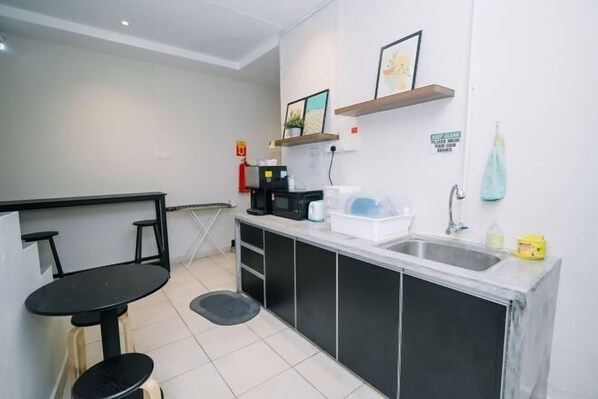 A compact kitchen with a black countertop, a sink, and a small dining area with stools. - Swing & Pillows at Penang Road, Georgetown (Northeast Penang Island)