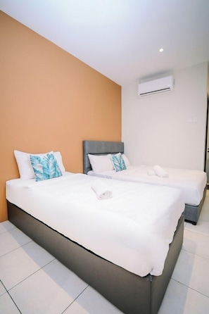 Habitación de hotel con dos camas, ropa de cama blanca y un cabecero gris.
