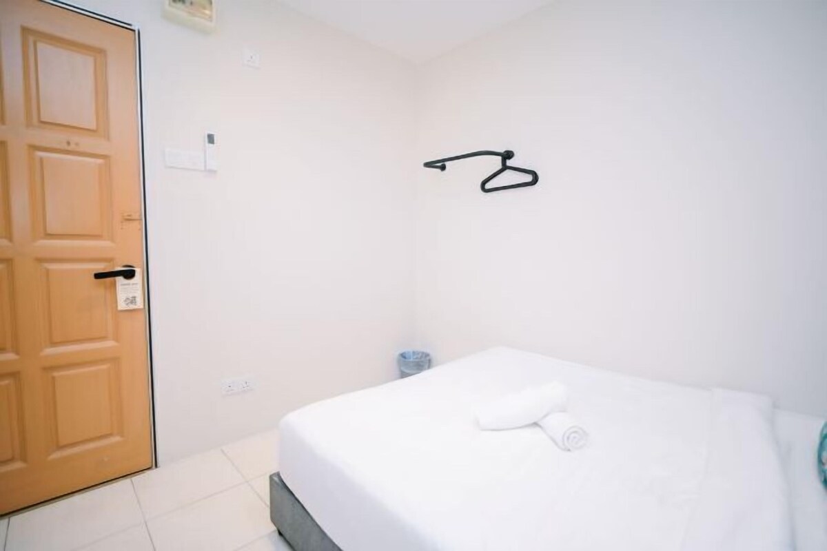 A hotel room with a bed, a wooden door, and a wall-mounted towel rack.