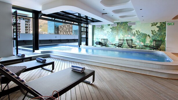 A modern indoor swimming pool with lounge chairs and a tropical mural. - Onyx Penthouse by ITC Hospitality (Cape Town)