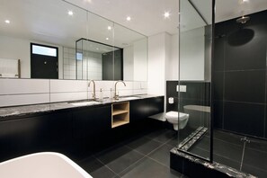 A modern bathroom with a large mirror, a bathtub, a toilet, and a glass-enclosed shower area.