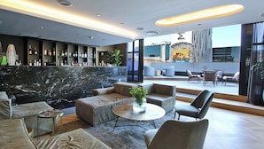 A modern lounge area with a marble reception desk, leather sofas, a round coffee table, and a view of the cityscape through large windows. - Onyx Penthouse by ITC Hospitality (Cape Town)