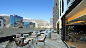 A rooftop terrace with modern seating, a bar area, and a view of city buildings and mountains. - Onyx Penthouse by ITC Hospitality (Cape Town)