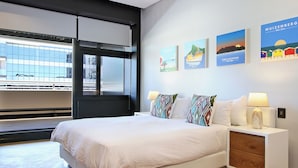 A modern hotel room with a large bed, a nightstand with a lamp, and a window with a view of a building. - Onyx Penthouse by ITC Hospitality (Cape Town)